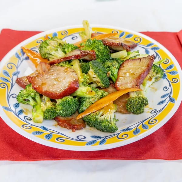 A colorful plate of Chinese BBQ pork with broccoli and carrots on a red napkin.