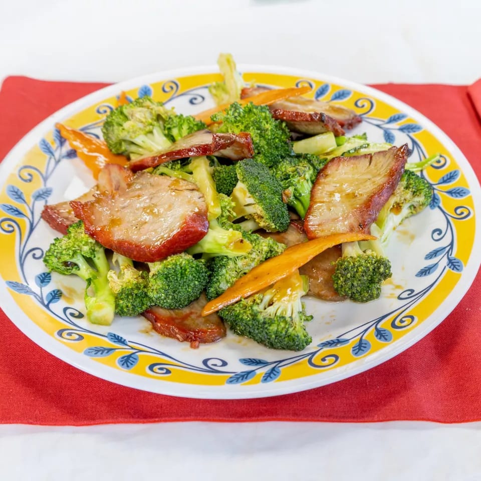 A colorful plate of Chinese BBQ pork with broccoli and carrots on a red napkin.