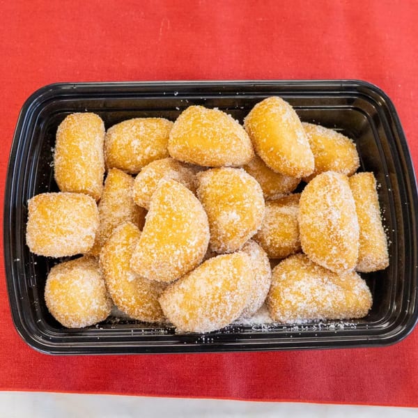 A black takeout container filled with golden-brown, sugar-dusted Chinese donuts on a red tablecloth.