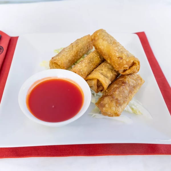 Golden-brown Chinese egg rolls with sweet and sour sauce on a white plate with red trim.