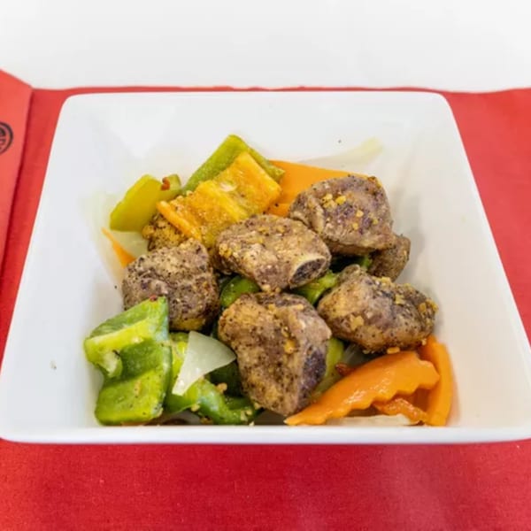 Salt and pepper pork ribs with green and orange bell peppers in a white dish.