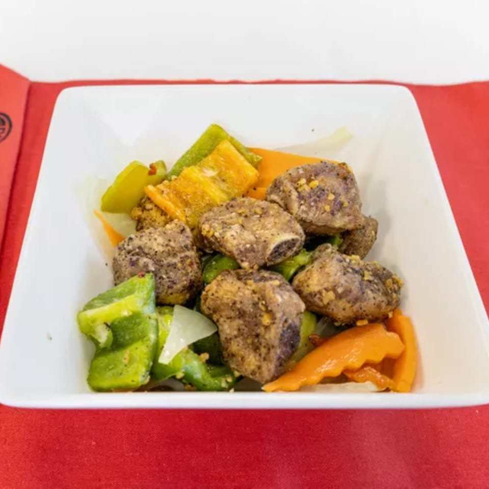 Salt and pepper pork ribs with green and orange bell peppers in a white dish.
