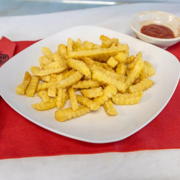 A white plate of golden crinkle-cut fries with seasoning, served with a side of ketchup.
