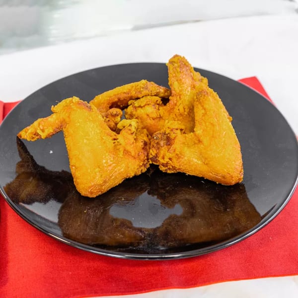 Golden-brown fried chicken wings, likely from China Bell Restaurant, arranged on a black plate with a red napkin.