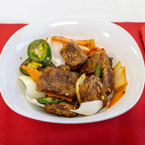 Spicy Chinese beef dish with onions, carrots, and sliced jalapeños in a white bowl.