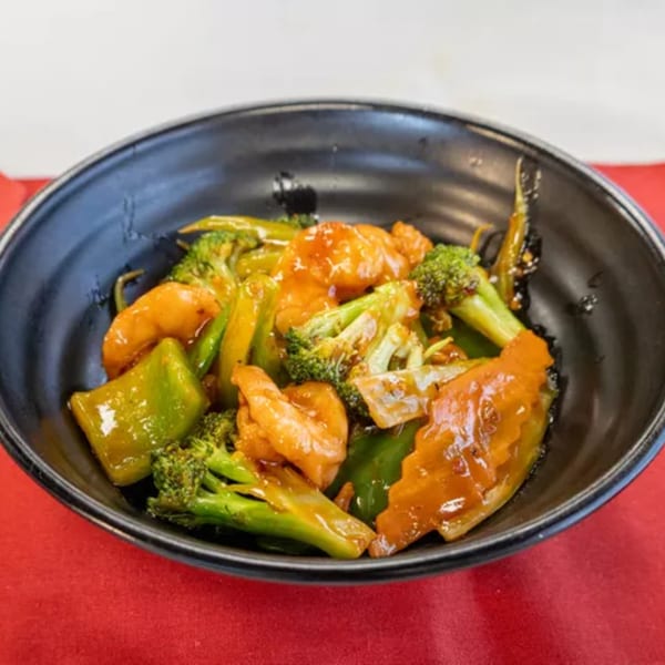 Shrimp and broccoli stir-fry with bell peppers in a black bowl on a red tablecloth.